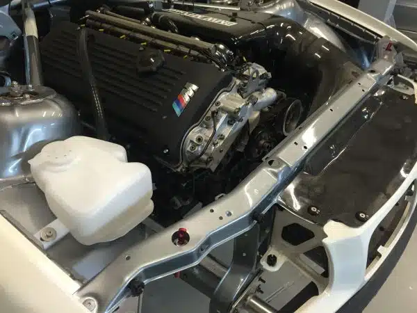 BMW engine installed in a car chassis, with a visible coolant reservoir.