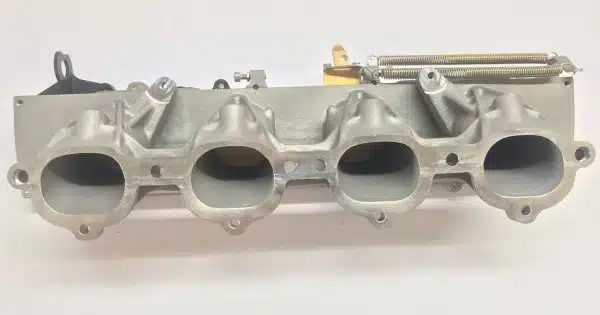 A silver automotive intake manifold with four ports on a white background.