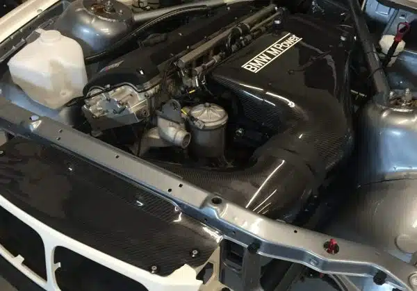 Car engine bay with a black intake system labeled "BMW M Power" and visible engine components.
