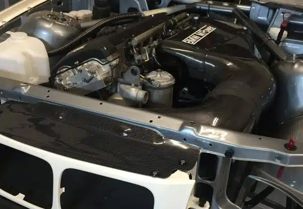 Car engine bay with various components and black intake piping visible.
