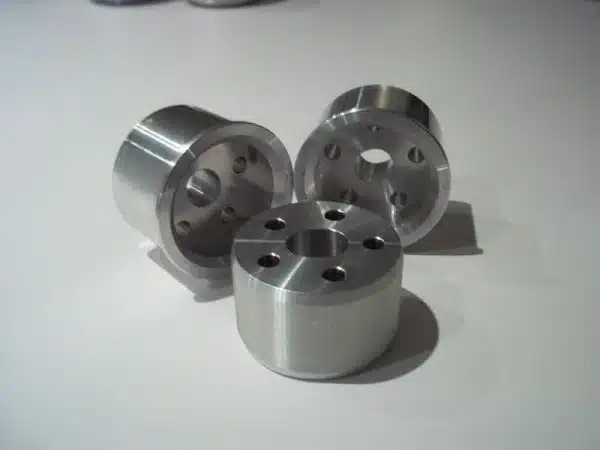 Three cylindrical aluminum bushings with holes, arranged on a white surface.