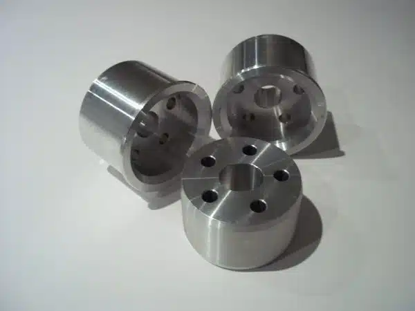Three cylindrical aluminum bushings with drilled holes, arranged on a white surface.