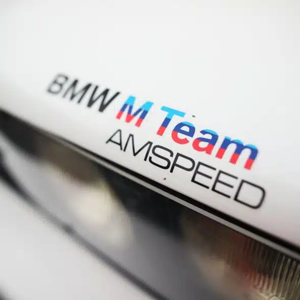 Close-up of a BMW M Team AMSPEED logo on a white car.