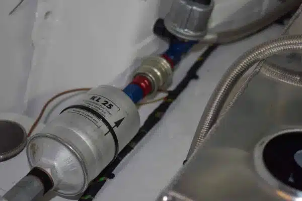 Metal fuel filter connected to pipes in an engine bay.