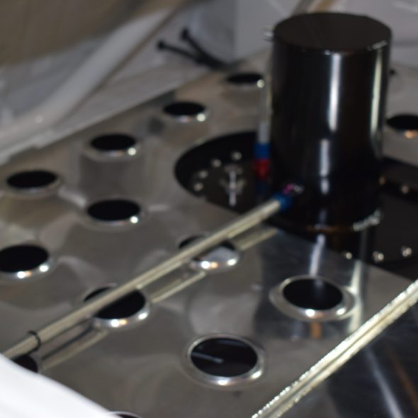 Metallic surface with circular holes and a black cylindrical component in the center.