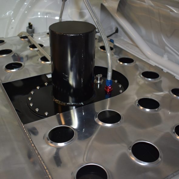 Metal fuel cell with circular cutouts and a black cylindrical component installed in a vehicle trunk area.