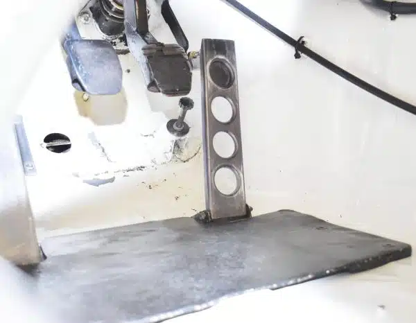 Car pedals and a metal footrest inside a vehicle with a white interior.