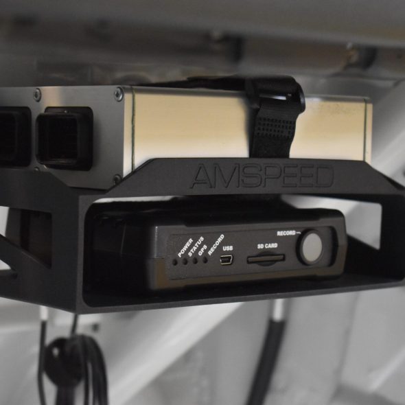 Black electronic device mounted on a metal frame inside a vehicle.