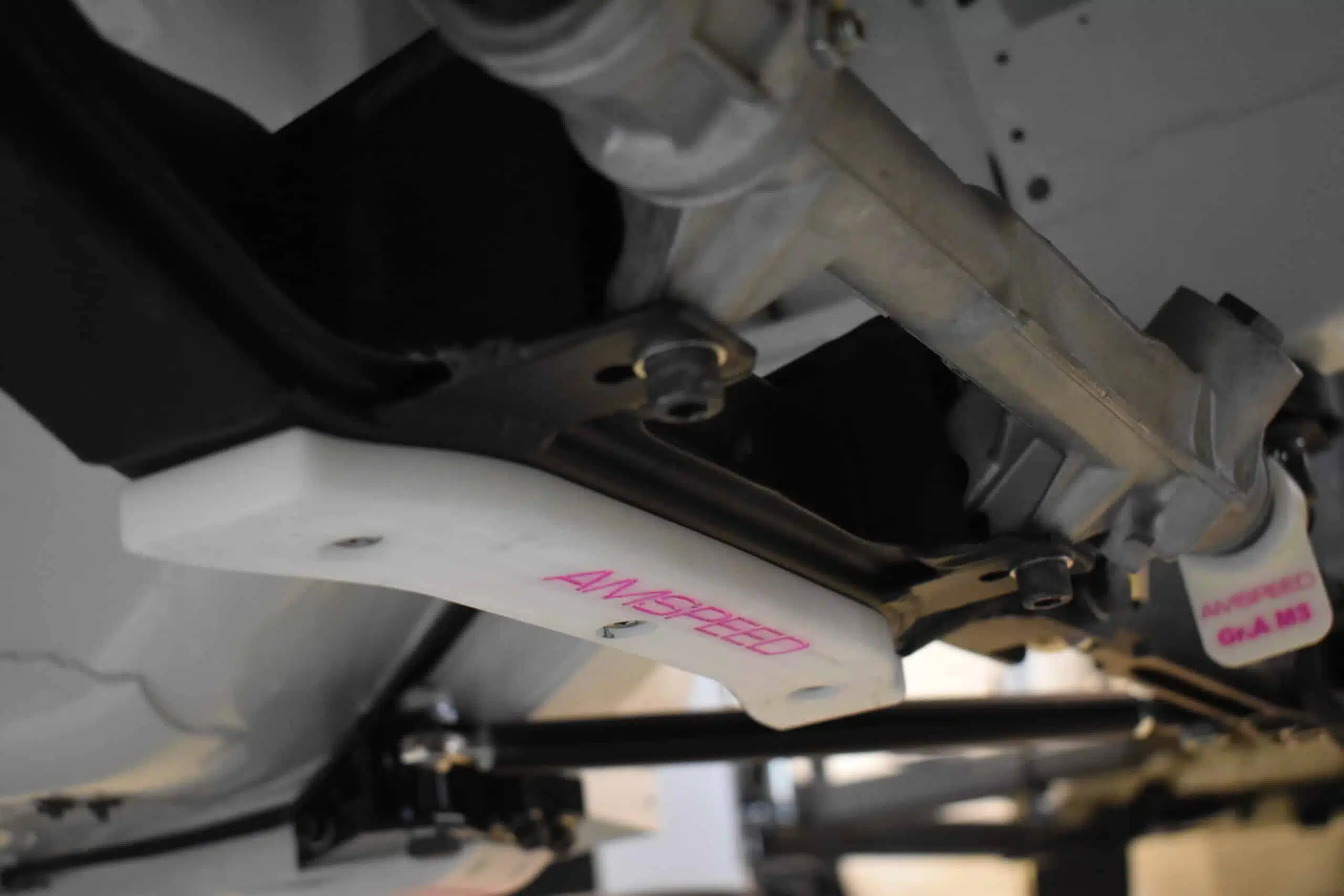 Close-up view of a car suspension component with a white bracket and pink lettering.