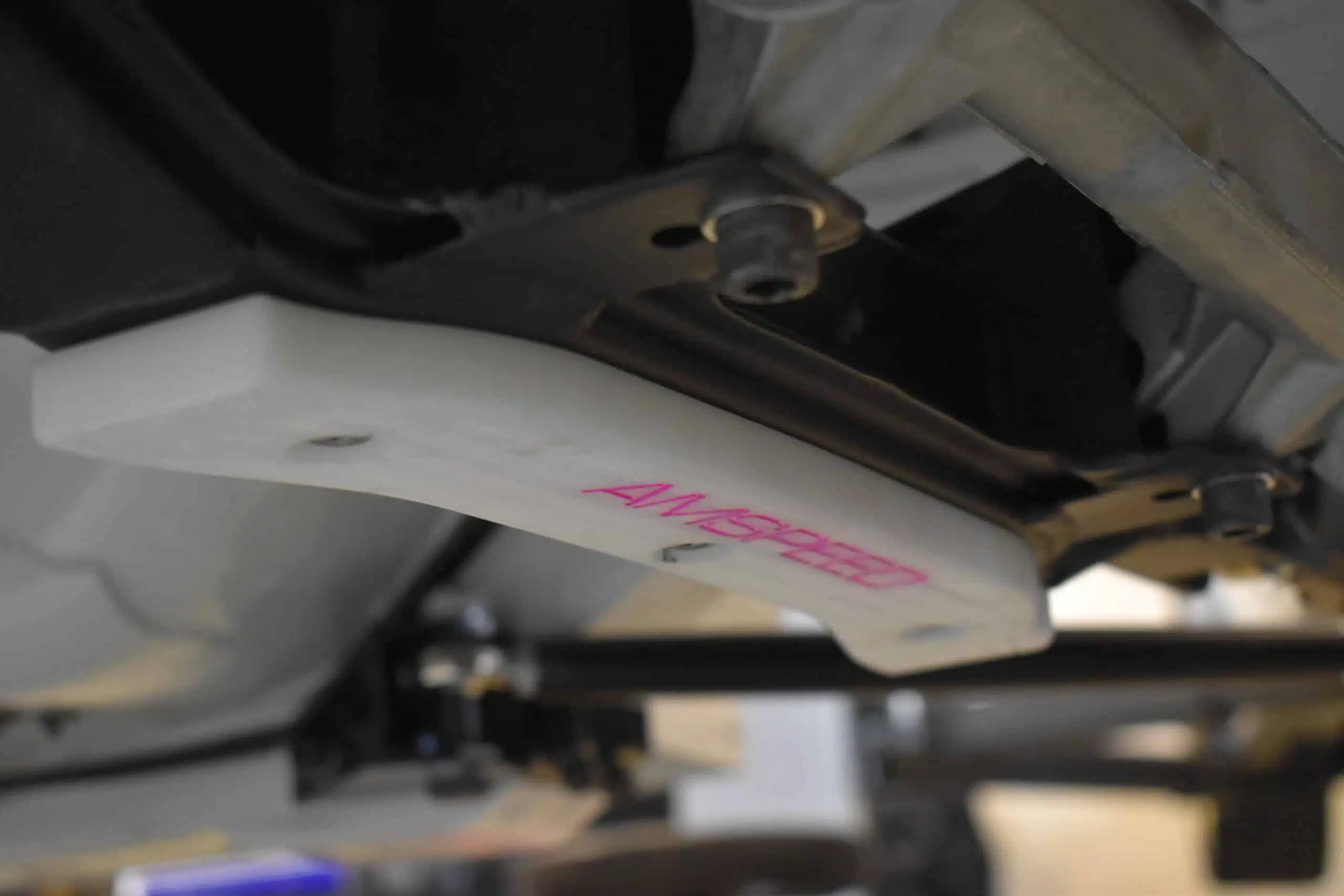 Close-up of a white plastic car part mounted under a vehicle chassis.