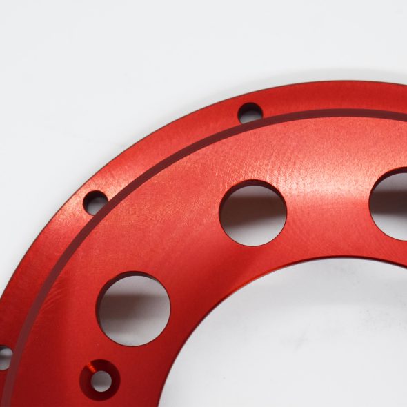 Red circular metal part with multiple holes, shown against a white background.