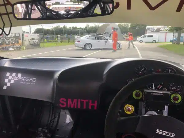 View from inside a race car of a stopped car and track marshals on a racetrack.
