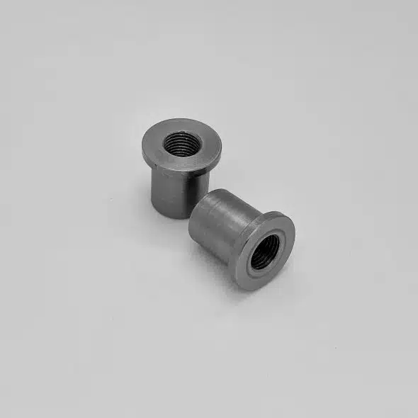 Two metal threaded inserts on a plain, light background.