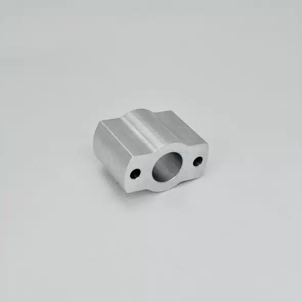 Small metal block with three holes placed on a plain light surface.