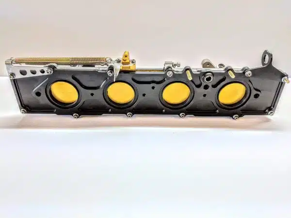 Black engine valve cover with four yellow caps, placed on a white background.