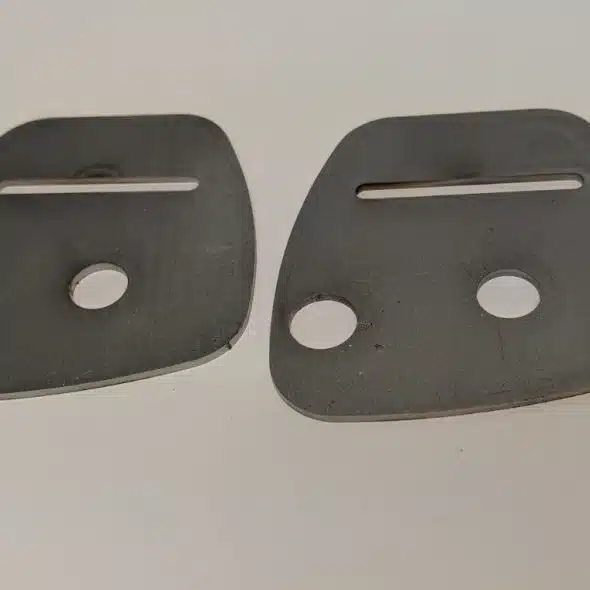 Two black, flat metal plates with holes and slots, placed side by side on a white surface.