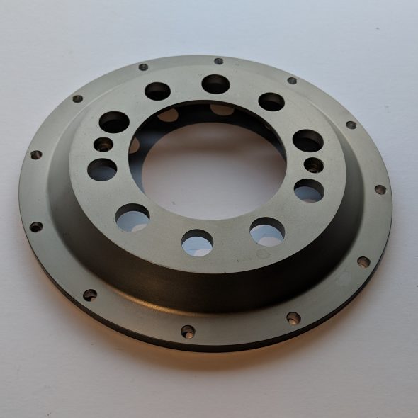 A metal circular machine part with multiple holes, lying on a plain surface.