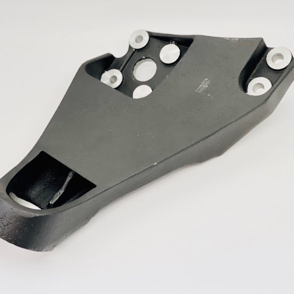 Black metal mechanical part with multiple circular holes and bolts, placed on a white surface.