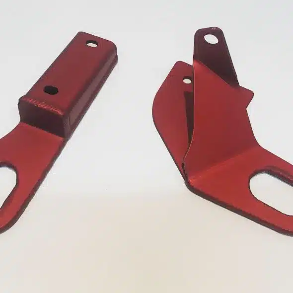 Two red metal brackets with oval holes are placed on a white background.