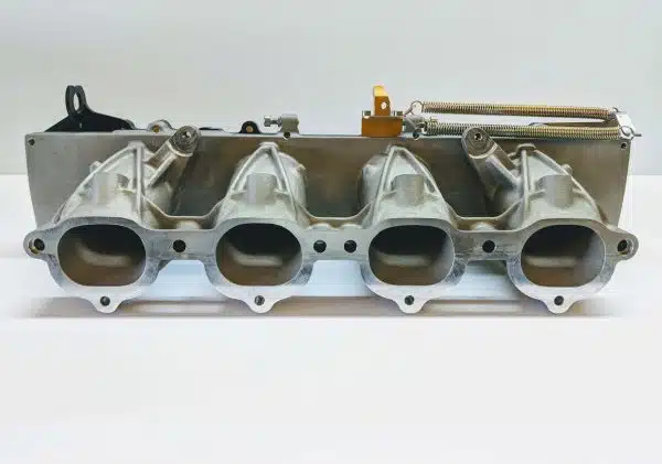 Metal car intake manifold with four ports on a white background.