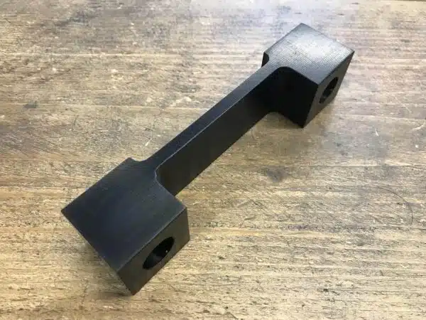 A black metal bracket with square ends on a wooden surface.