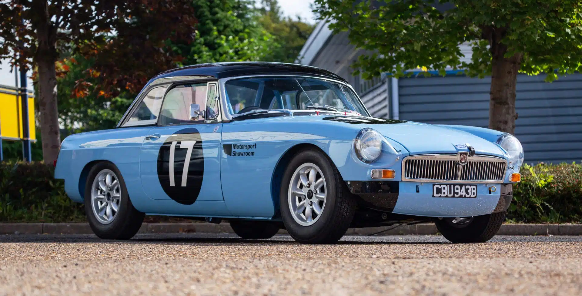 Light blue vintage MGB race car with number 17 parked outdoors.